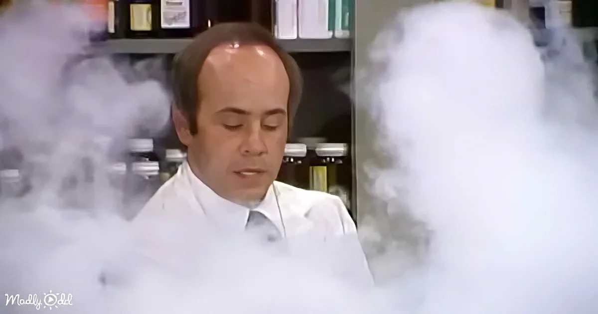 A man in a white lab coat stands amidst swirling white smoke in a laboratory setting.
