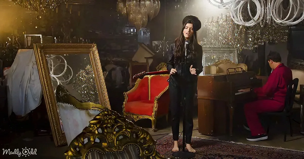 A woman sings into a microphone in a room filled with ornate furniture and chandeliers.