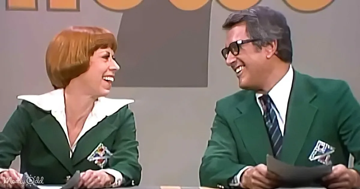 A man and woman in green suits smile and laugh together, seated at a table.