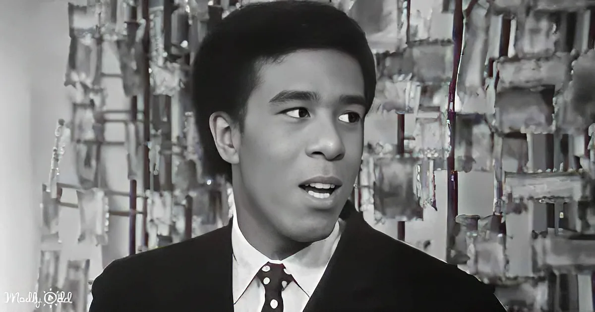 A man in a suit and tie, looking to the side, with a black-and-white background of shelves.