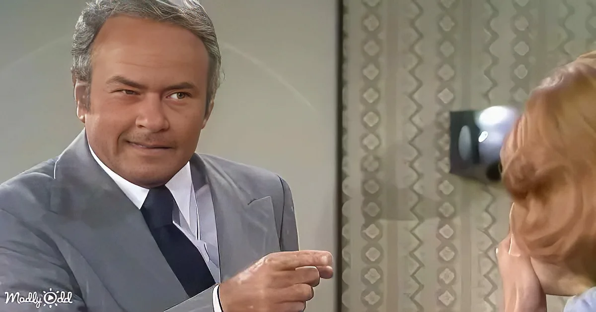 A man in a suit and tie gestures while talking to a woman with blonde hair.