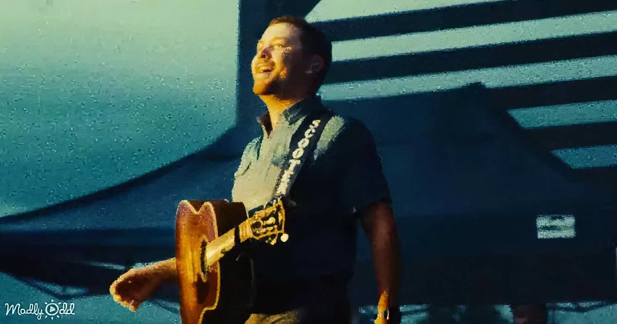 A man in a blue shirt plays a guitar on stage, smiling with his eyes closed.