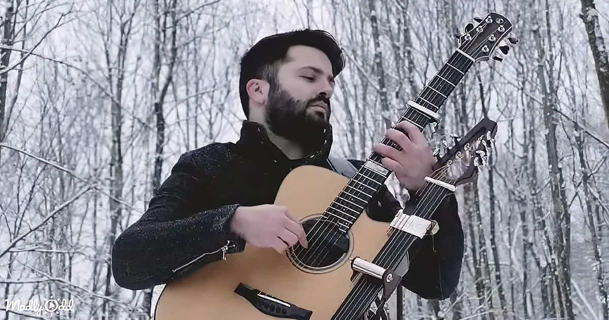A man with a beard plays an acoustic guitar in a snowy forest.