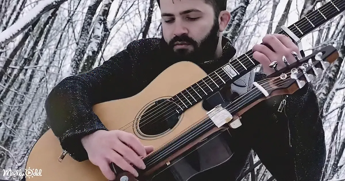 A man with a beard plays an acoustic guitar in a snowy forest setting.