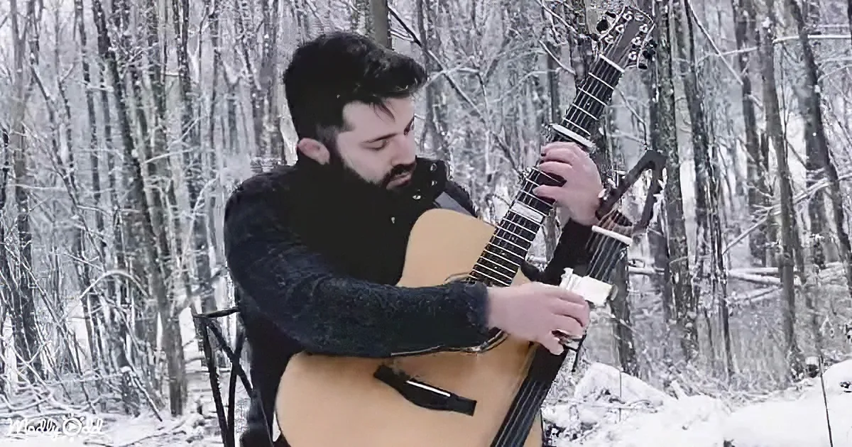 A man plays a guitar in a snowy forest, surrounded by snow-covered trees.
