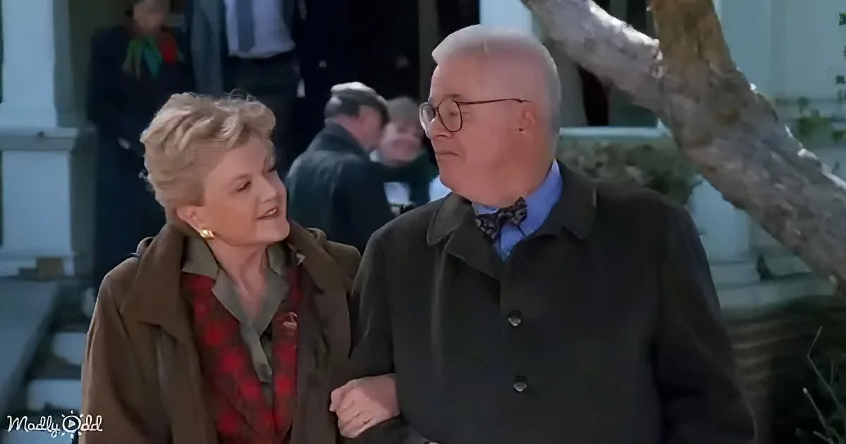 A man and woman walk together, the man in a dark coat and bow tie, the woman in a plaid shirt and brown jacket.
