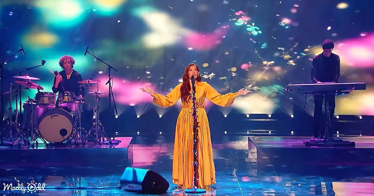 A woman in a yellow dress sings on stage with a colorful, illuminated backdrop and musicians.