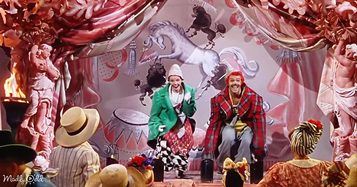 Two performers in vibrant costumes dance on a whimsical stage with a horse backdrop and ornate decorations.