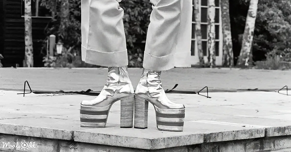 A person stands on a stage wearing shiny, metallic platform boots and a white outfit.