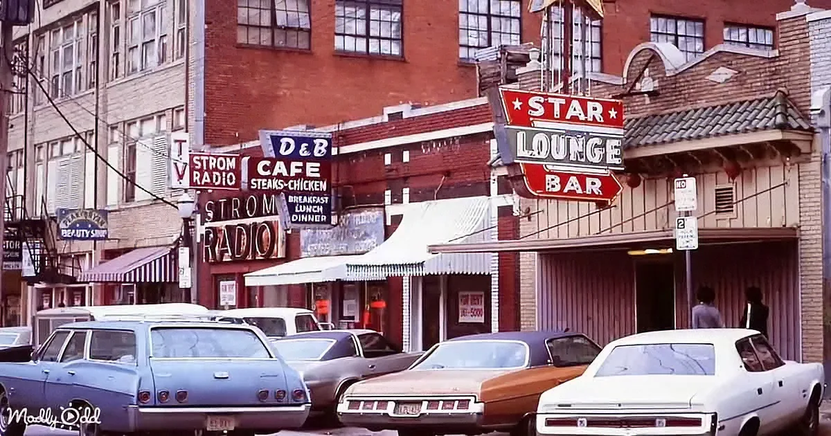 Vintage street scene with classic cars, "Strom Radio," "D&B Cafe," and "Star Lounge Bar" signs.