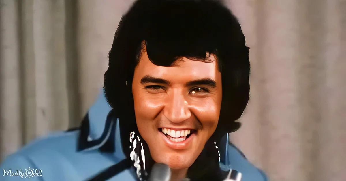 Elvis Presley smiles widely, wearing a blue suit with large earrings, against a blurred background.