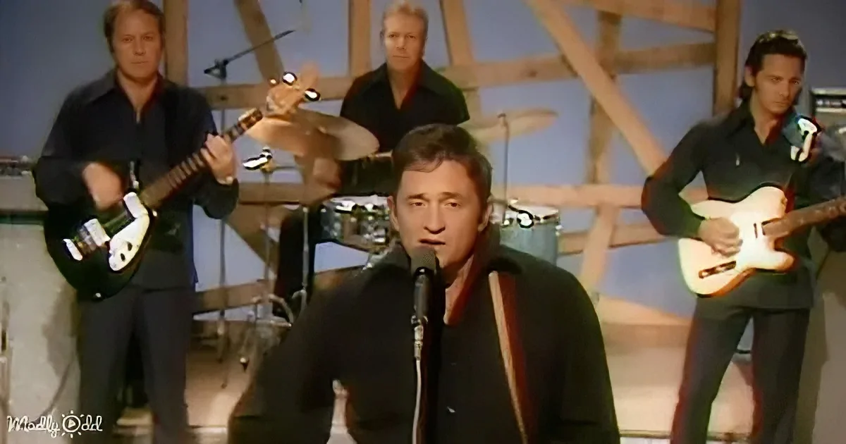 A man sings into a microphone, surrounded by musicians playing guitars and drums.