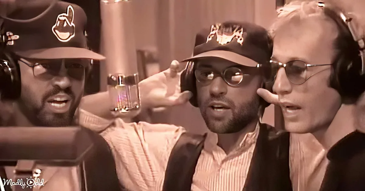 A man in a striped shirt and cap is surrounded by two others, all wearing headphones, in a recording studio setting.