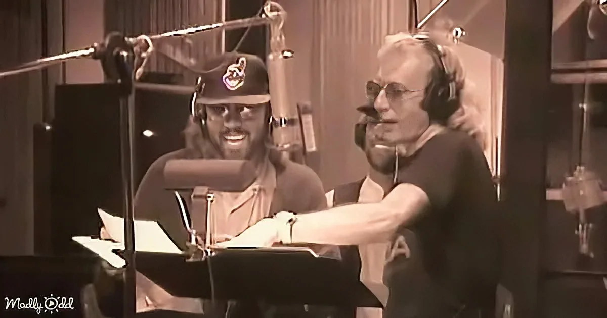 Two men in a recording studio, one adjusting headphones, both smiling.