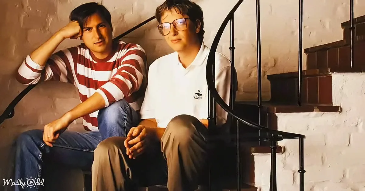 Two individuals sit on a spiral staircase, one in a striped shirt and jeans, the other in a white polo shirt and khaki pants.