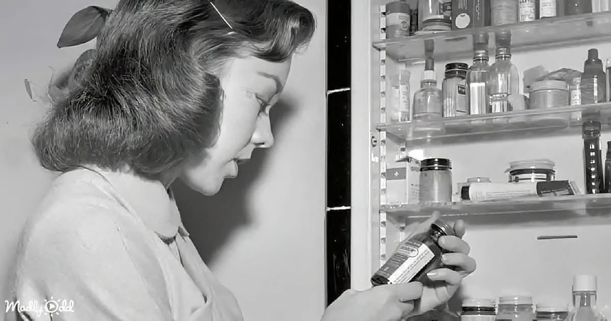 Woman examines medicine bottle in open medicine cabinet filled with various bottles and jars.
