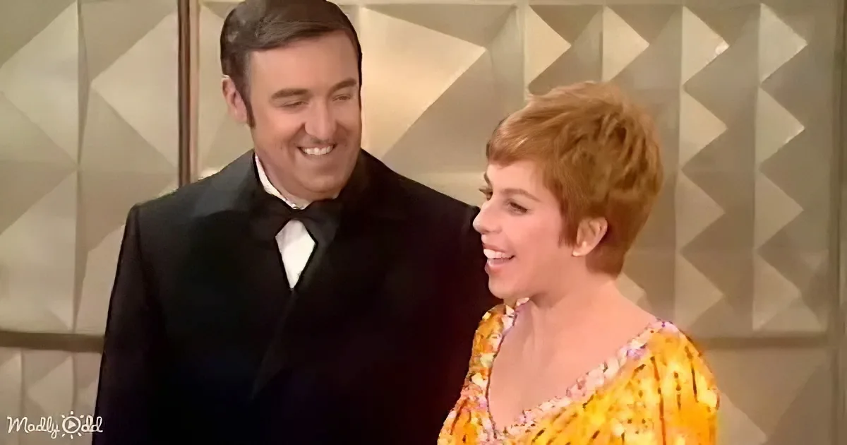 A man in a tuxedo and a woman in a floral dress share a joyful moment, smiling at each other.