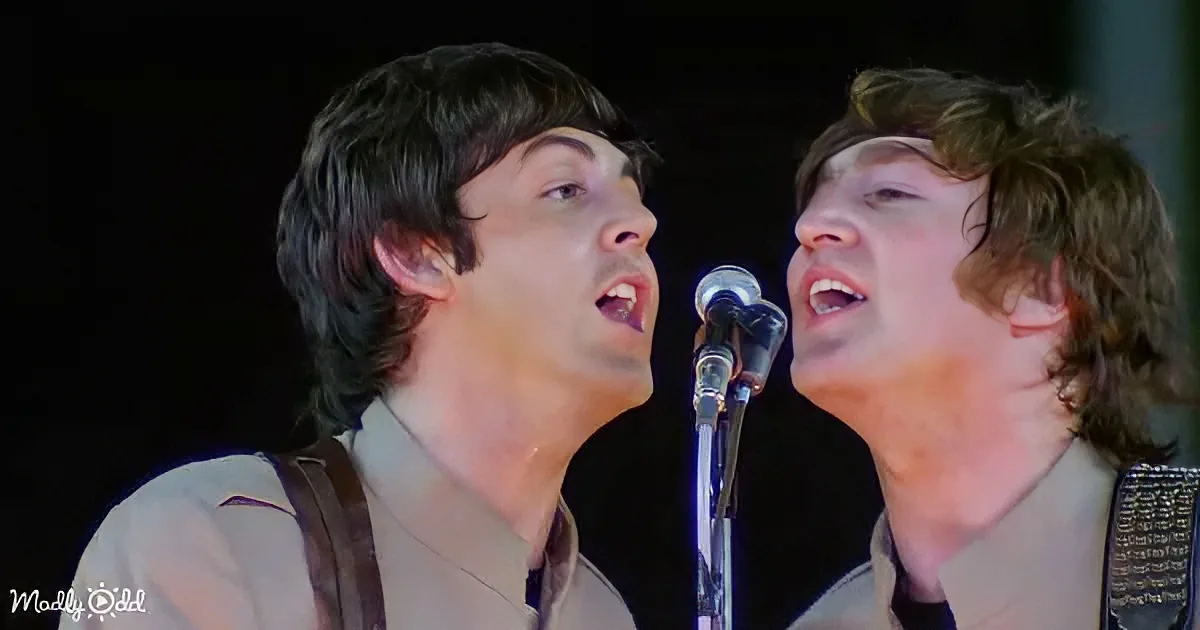 Two men sing passionately into a microphone on stage, their expressions intense.