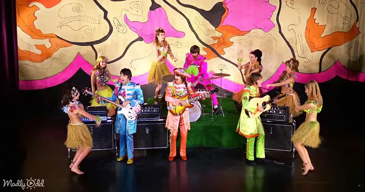 A band in colorful costumes performs on stage with dancers in grass skirts.