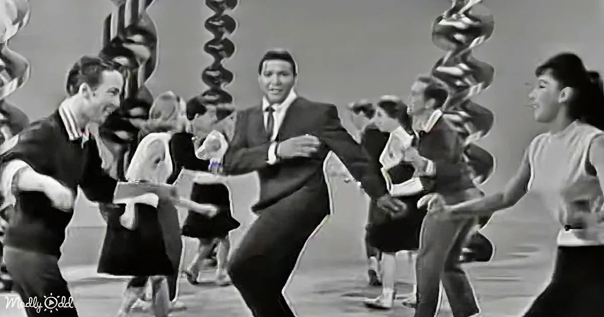 A man in a suit dances energetically with a group of people in a lively setting.