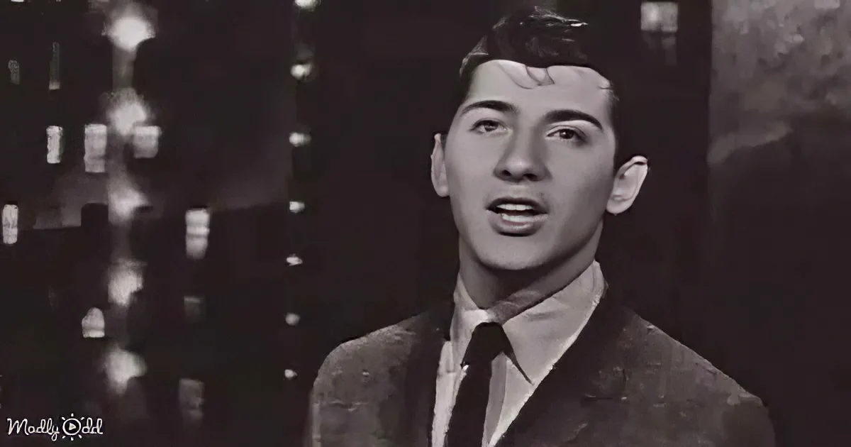 A man in a suit and tie, possibly singing, with a blurred background.