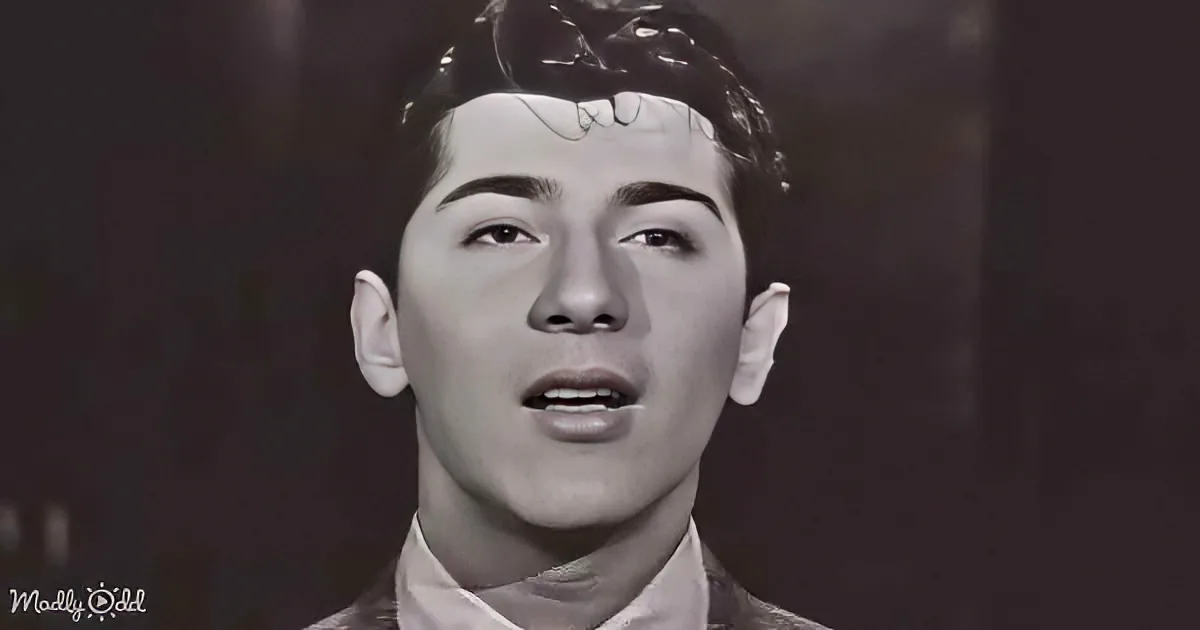 A young man with short, styled hair and a white shirt is captured in a close-up shot, looking upwards with a serious...