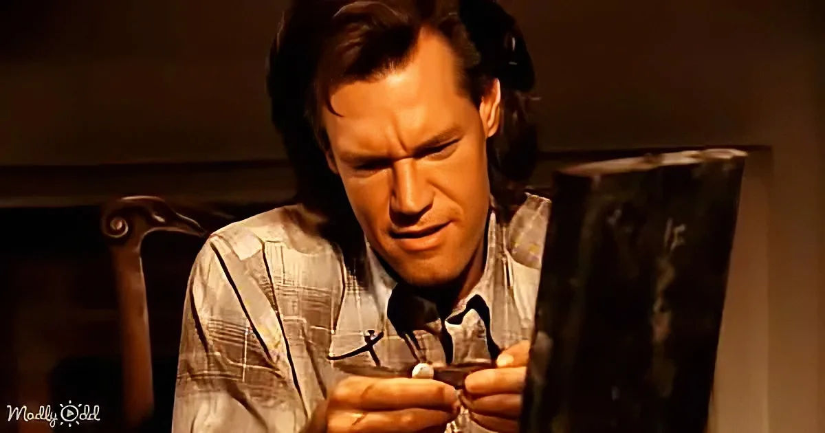 A man with long hair and a plaid shirt is intently examining a small object in his hands.