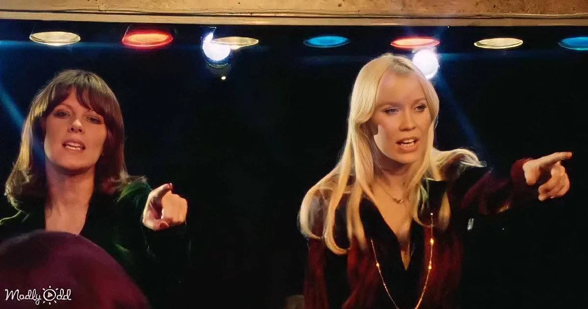 Two women with expressive gestures and colorful stage lighting behind them.