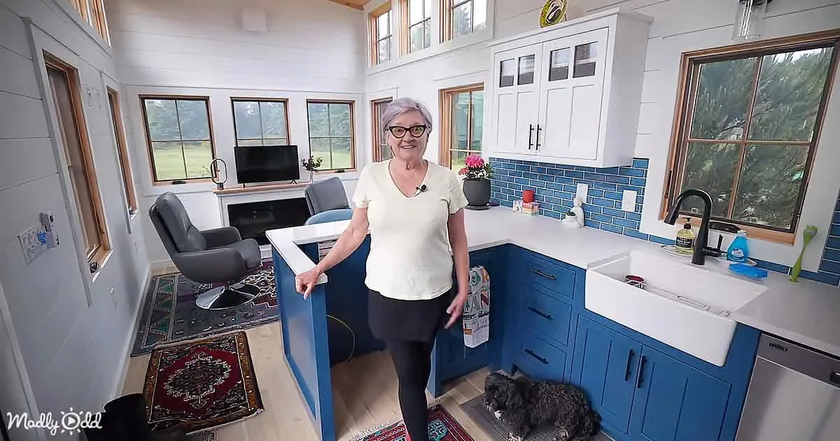 A woman stands in a modern kitchen with blue cabinets, white countertops, and a dog on the floor.
