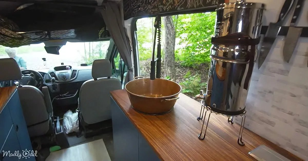 A van interior with a wooden countertop, a copper pot, and a stainless steel water heater.