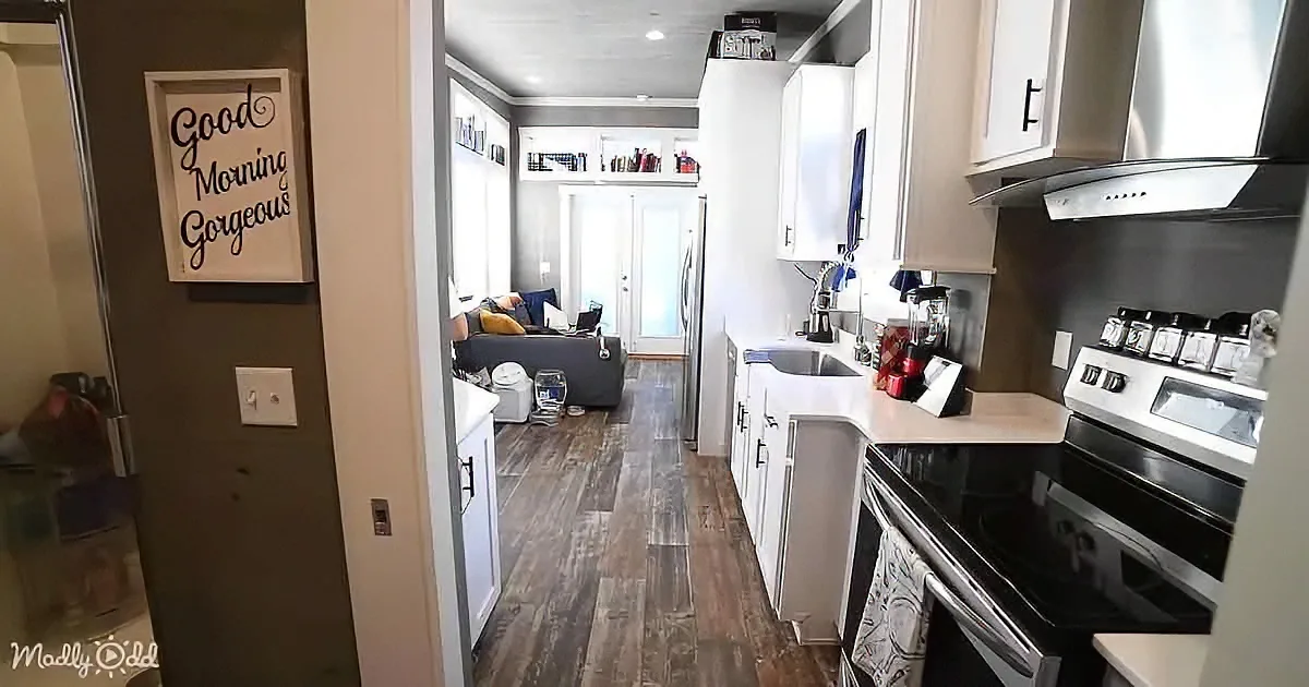 A cozy kitchen with white cabinets, stainless steel appliances, and a "Good Morning Gorgeous" sign on the wall.