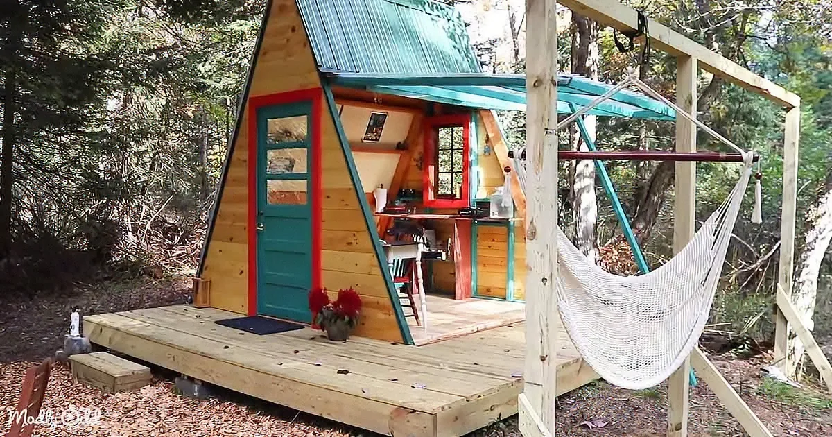 A cozy, colorful A-frame cabin with a hammock and wooden deck in a forest setting.