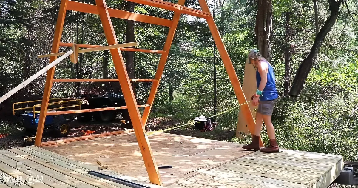 A person measures a wooden structure in a forested area with tools and a vehicle nearby.