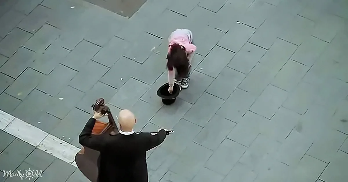 A person in a black suit and white hat is pointing at another person in a pink hat and black outfit who is bending over a...