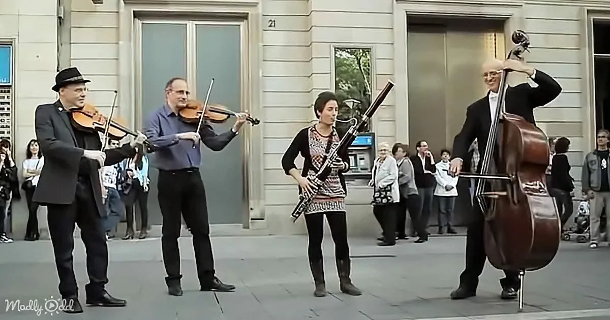 A quartet of musicians plays outdoors, with two violinists, a bassoonist, and a cellist, while spectators watch.