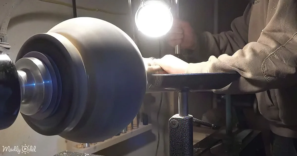 A person uses a flashlight to inspect a spinning metal object on a lathe.
