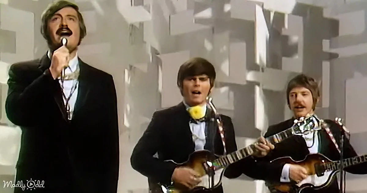 A man in a suit sings into a microphone, accompanied by two musicians playing guitars.