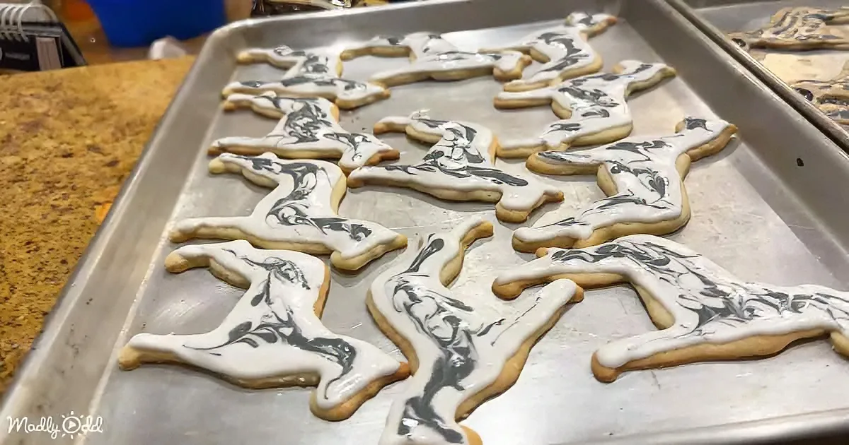 Reindeer-shaped cookies with white icing and black swirls on a baking sheet.