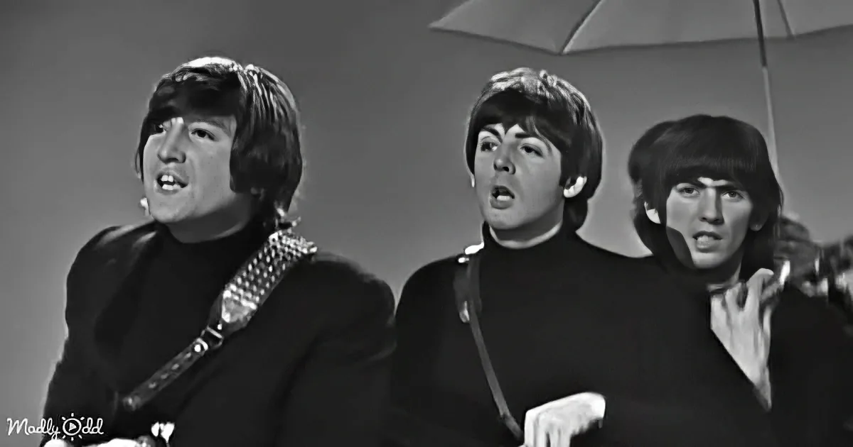 The Beatles perform on stage, dressed in black, with one member playing guitar and another holding an umbrella.