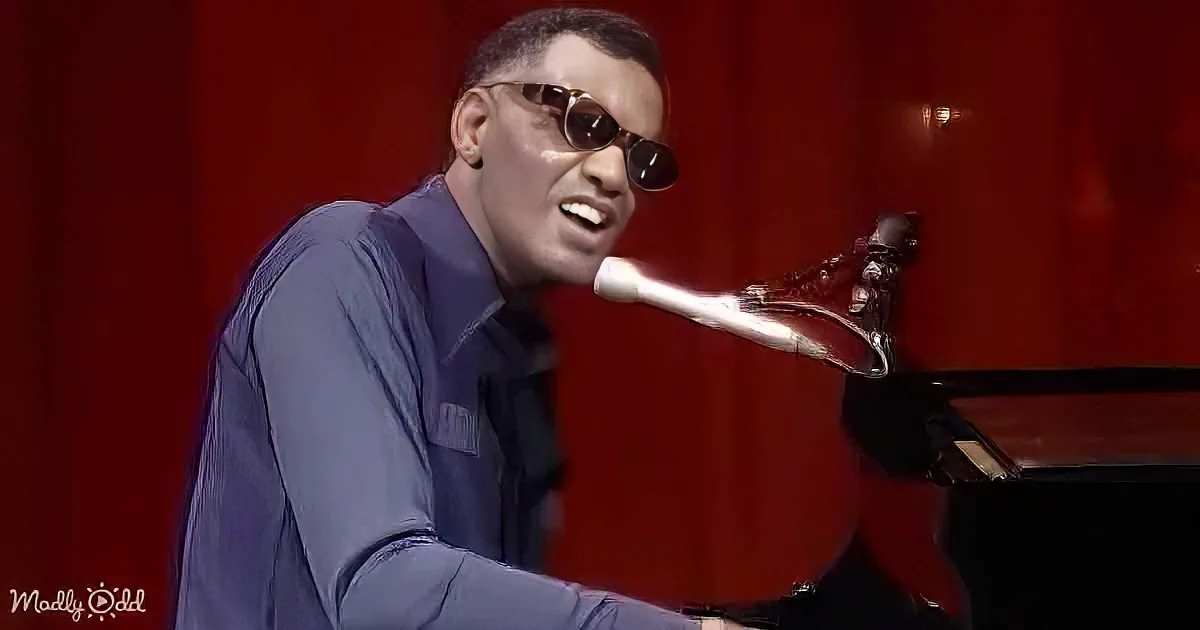 A man in a blue shirt and sunglasses is playing a piano with a microphone in front of him.