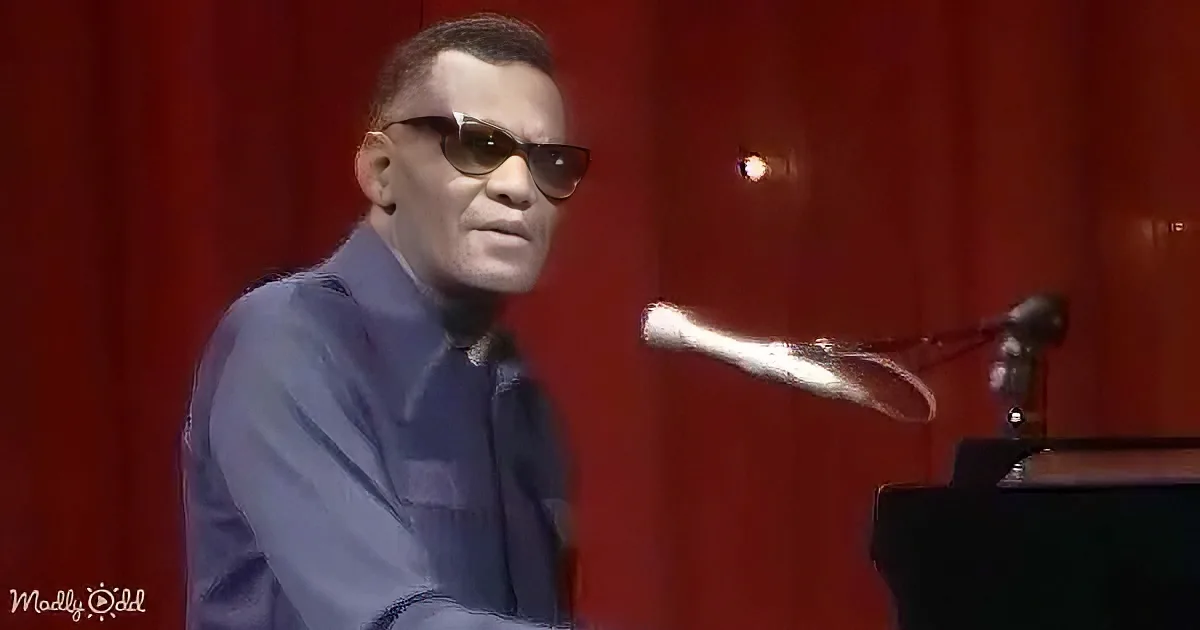 A man in a suit and sunglasses sits at a piano in a red-lit room, with a microphone in front of him.