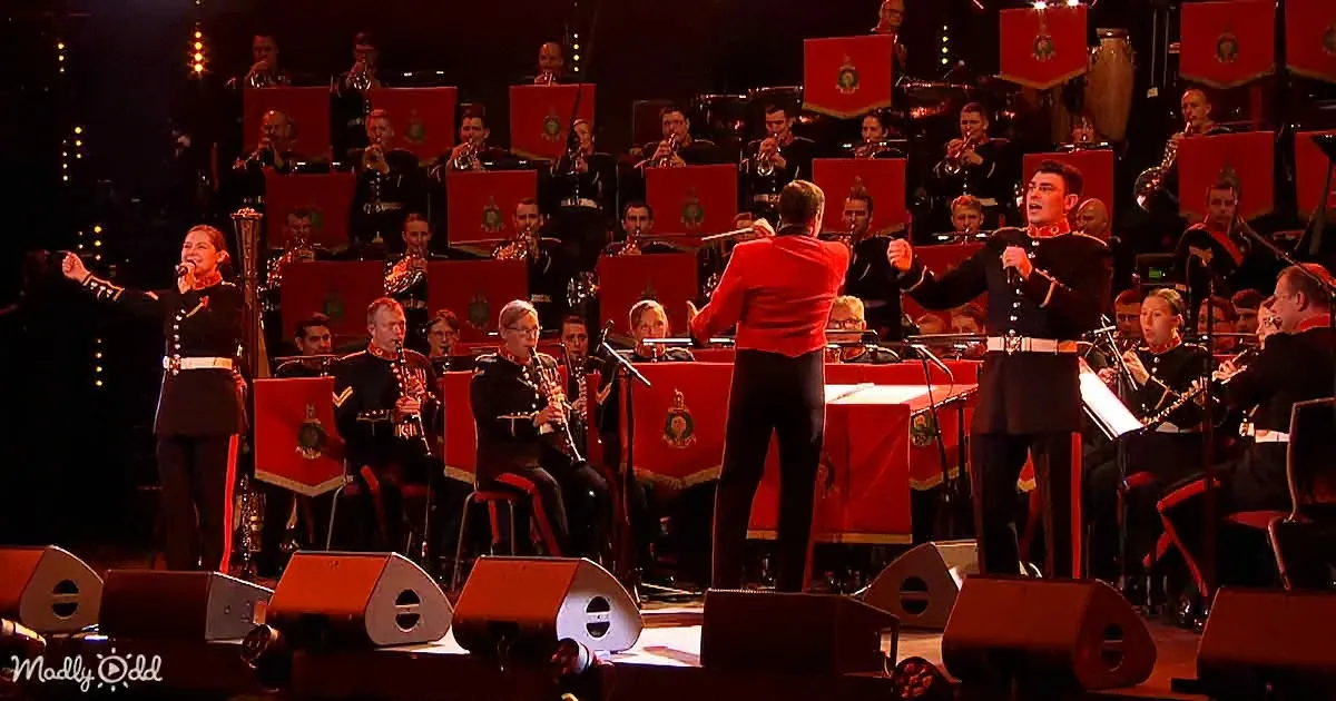 A conductor leads a military band with red banners and uniformed musicians.