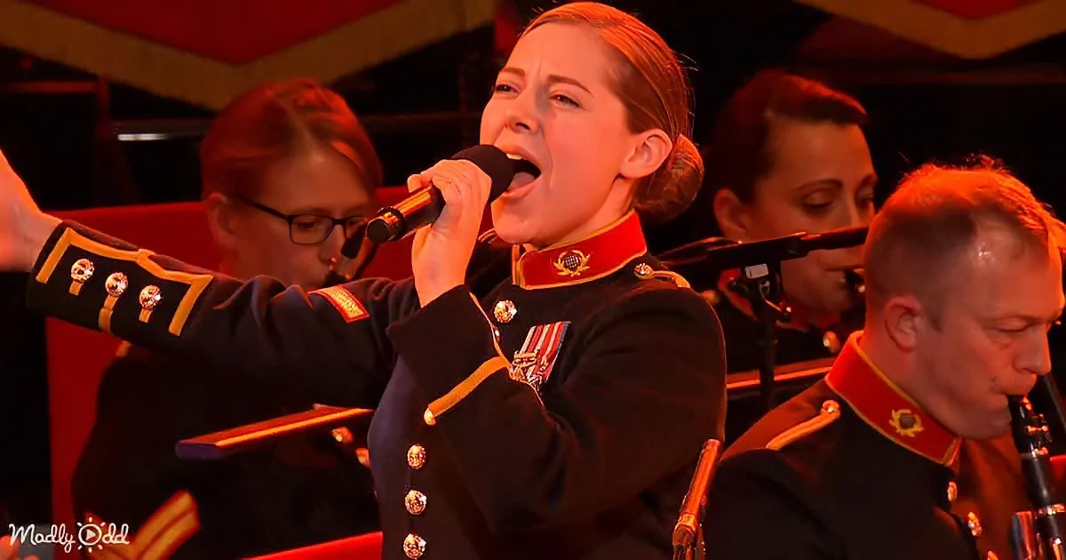 A woman in a military uniform sings into a microphone, surrounded by musicians in similar attire.