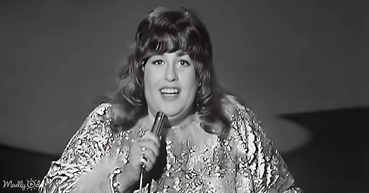 A woman in a sparkly dress holds a microphone, singing with a microphone in her hand.