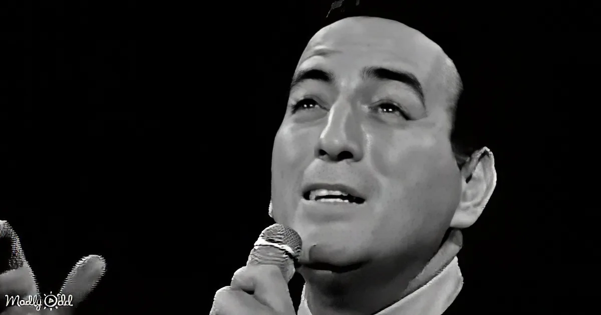A man sings into a microphone, his eyes closed, against a dark background.