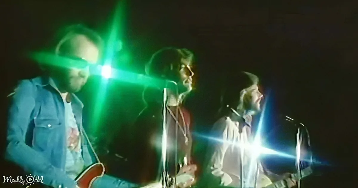 A band performs on stage with bright stage lights creating lens flares.