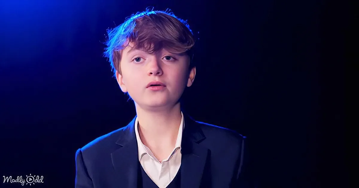 A person in a suit with a white shirt, standing against a dark background with blue lighting.