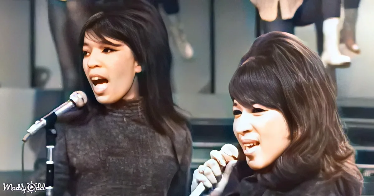 Two women sing into microphones, one with long dark hair, the other with bangs, in a performance setting.