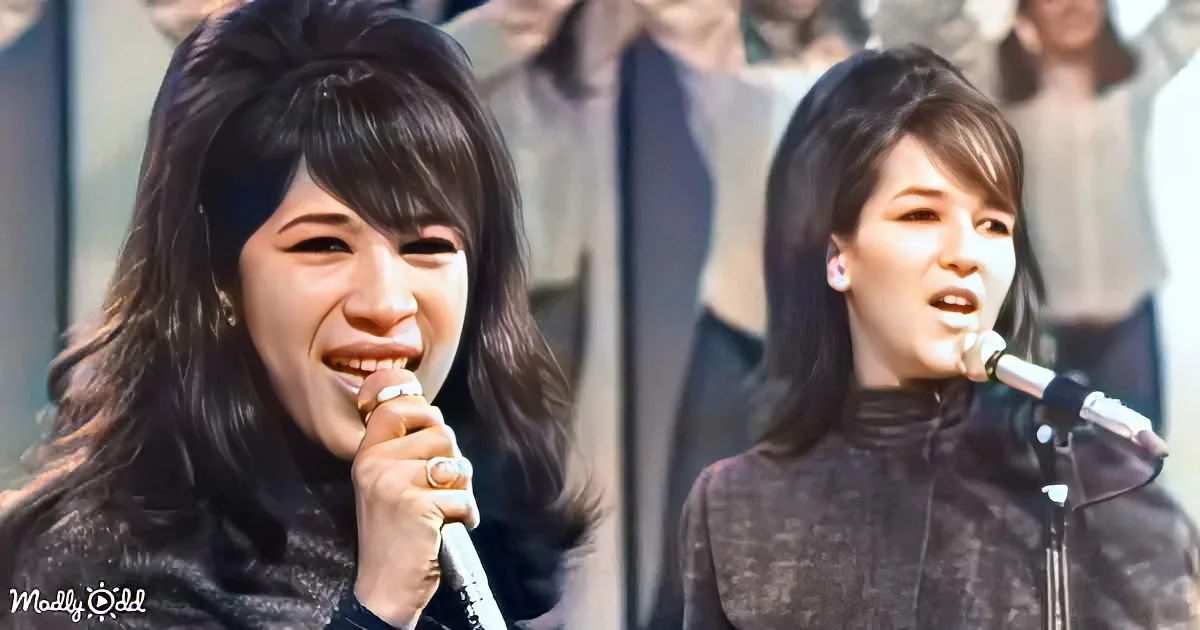 A woman with long dark hair smiles while holding a microphone, singing on stage.