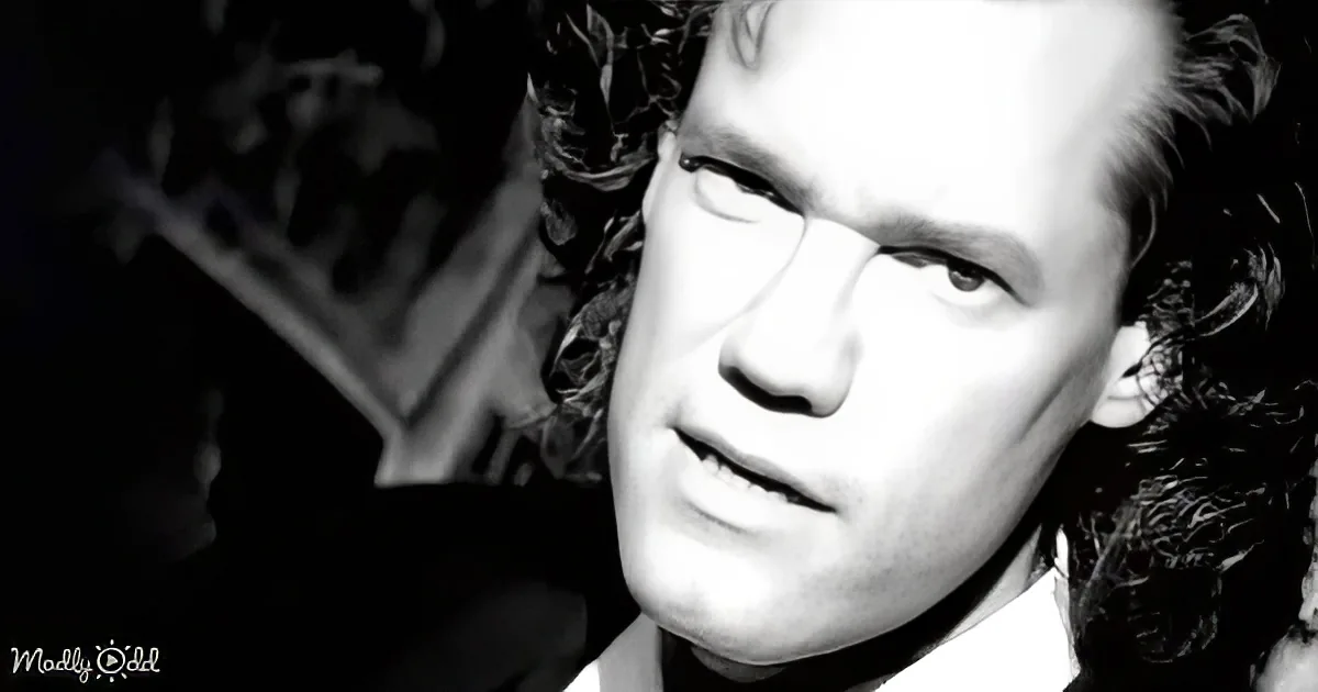 A man with curly hair and a serious expression, wearing a suit, is the main subject of this black and white image.